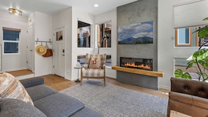 Een moderne woonkamer met een open haard, een bank, een fauteuil en een groot raam.