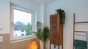 A bathroom with a window, a wooden shelf with towels, a potted plant, and a wall-mounted towel rack. - Stylish design apartment in Langenbach, near Munich and Munich Airport (Langenbach)