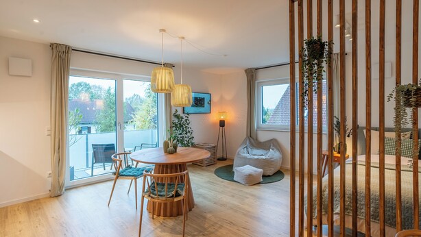 Ein modernes Wohnzimmer mit einem Holzesstisch, Stühlen, einem Sitzsack und einem großen Fenster, das einen Ausblick nach draußen bietet.