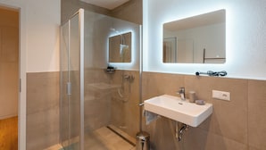 Ein modernes Badezimmer mit einer gläsernen Duschkabine, einem weißen Waschbecken und einem Spiegel mit integrierter Beleuchtung.