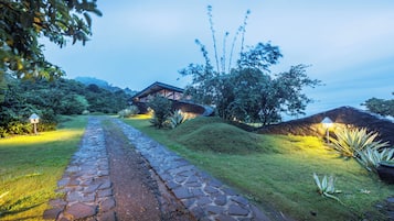 Un sendero de piedra conduce a un edificio rústico rodeado de exuberante follaje y bambú.