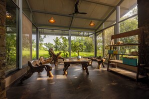 A spacious room with a large glass wall, wooden furniture, and a ceiling fan. - TAALISH - A BOUTIQUE RESORT (Junnar)
