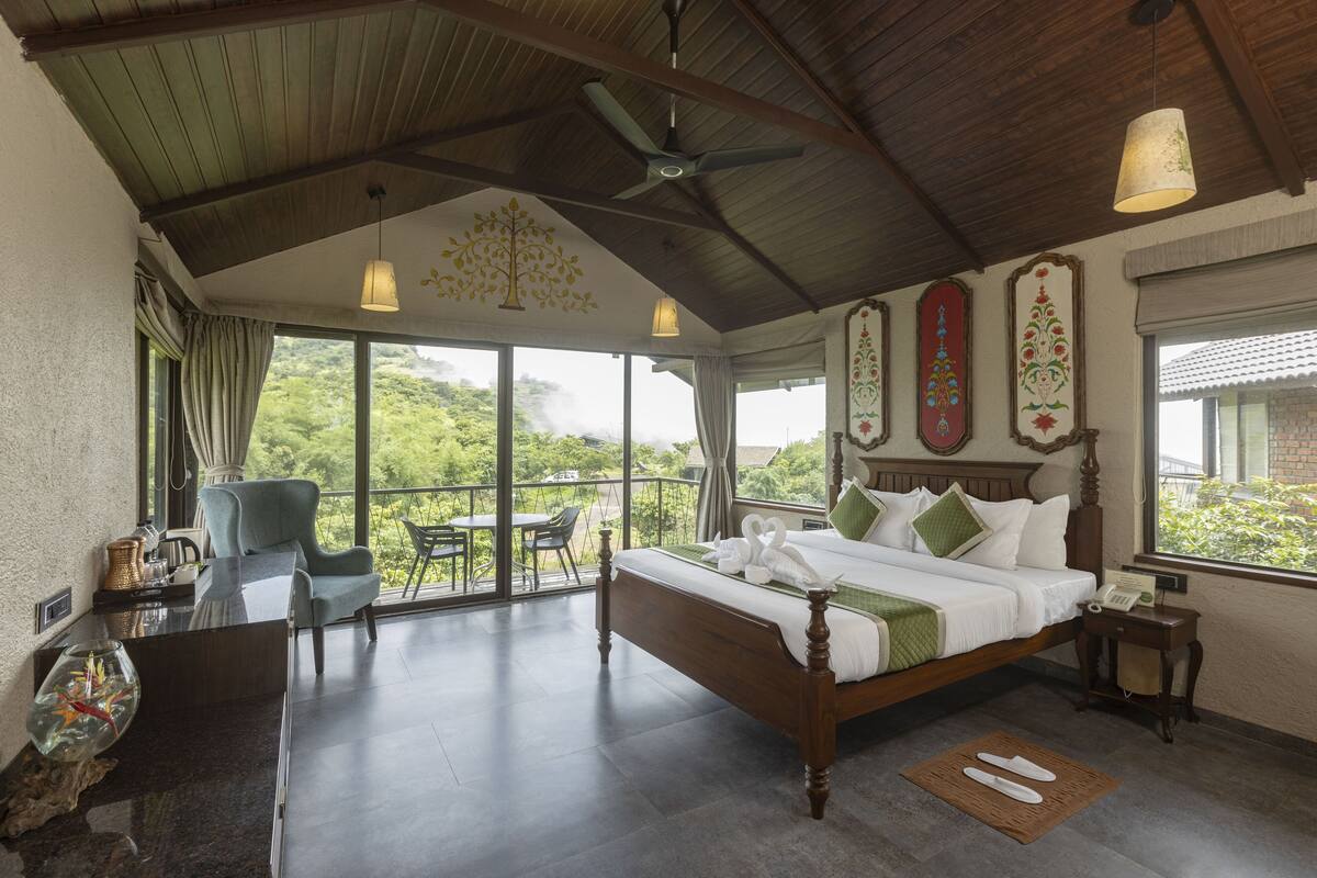 Un dormitorio amplio con una cama grande, un escritorio y una silla. Cuenta con un balcón con vistas a zonas verdes.