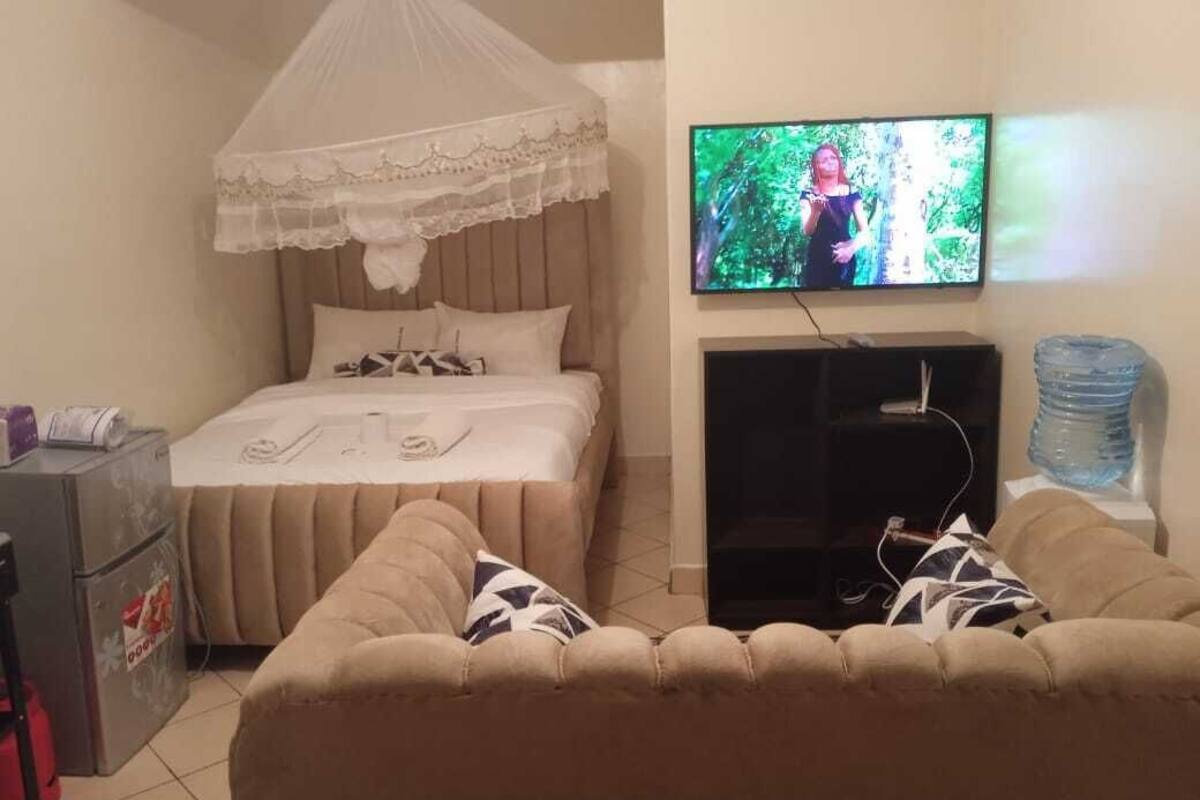 A bedroom with a bed, a TV, a water dispenser, and a sofa.