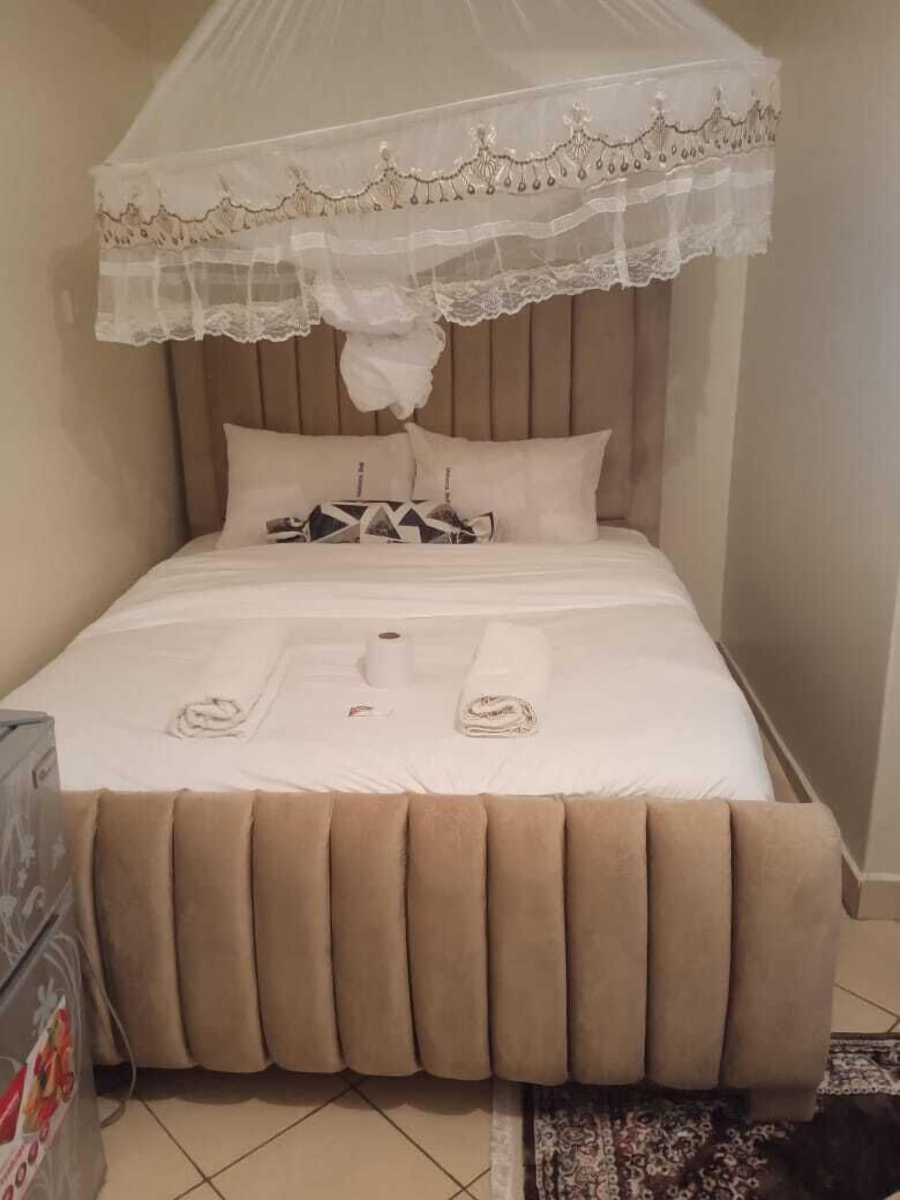 A neatly made bed with a canopy, pillows, a rolled towel, and a toilet paper roll.