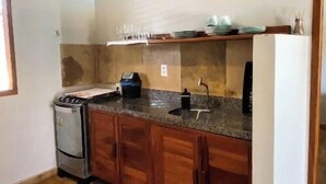 A kitchen with wooden cabinets, a granite countertop, a stove, and a hanging light fixture. - Vila Flamboyant (Cajueiro da Praia)