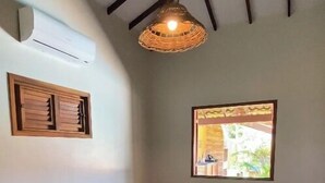 A bedroom with a bed, a window, a hanging light fixture, and a wall-mounted air conditioner. - Vila Flamboyant (Cajueiro da Praia)