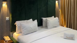 Una camera d'albergo con un letto grande, una testiera verde, biancheria da letto bianca e un telefono sul comodino.
