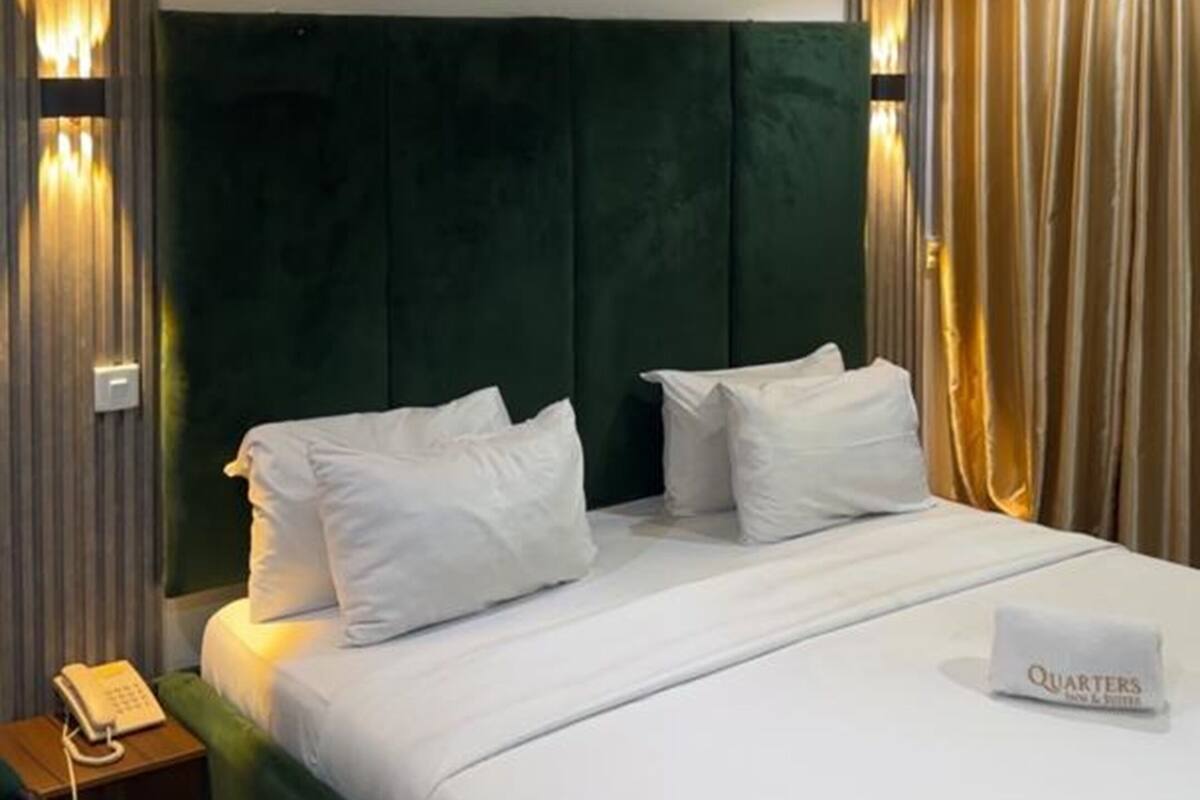 Una habitación de hotel con una cama grande, cabecera verde, ropa de cama blanca y un teléfono en la mesita de noche.