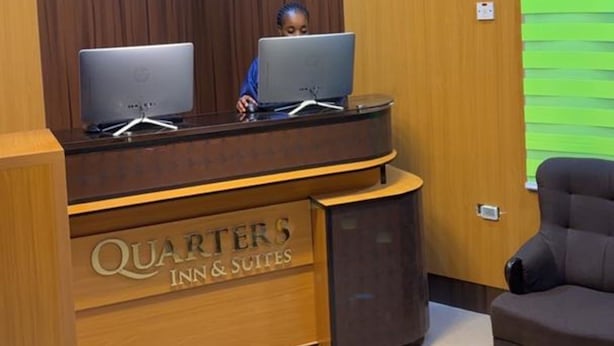 Una reception con due computer, un lampadario moderno e un cartello con la scritta 'QUARTERS INN & SUITES'.