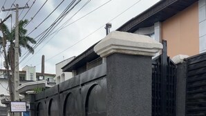 Un ingresso recintato con un pilastro in cemento e un cancello in metallo, che conduce a un edificio con facciata beige.