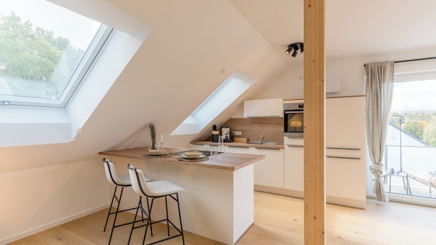 Una cocina moderna con una isla central, dos taburetes de bar y vistas al exterior a través de amplias ventanas.