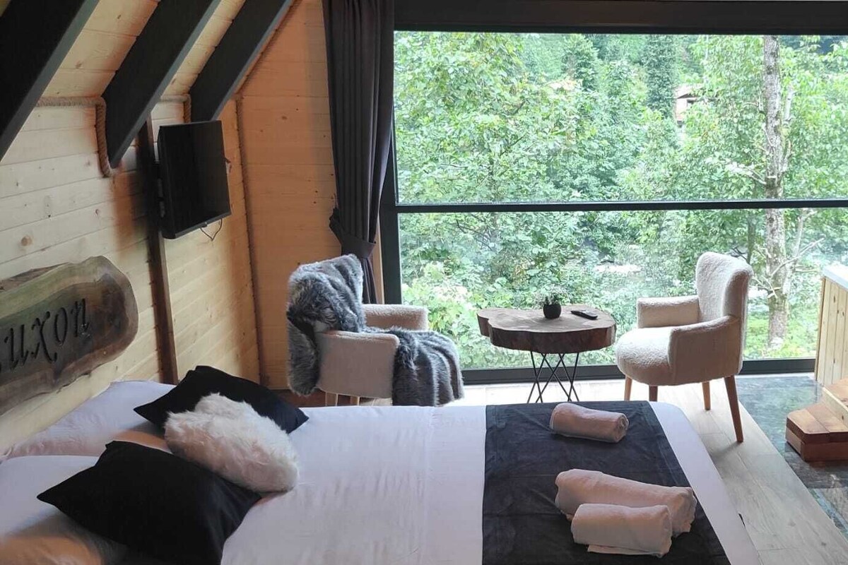 Uma cabana aconchegante com cama, duas cadeiras, uma mesa pequena e uma banheira de hidromassagem.