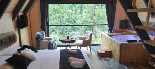Una cabaña acogedora con una cama, dos sillones, una mesita y un jacuzzi.
