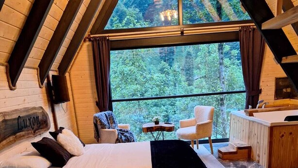 A cozy loft bedroom with a large window, a bed, a chair, and a small table. - Luxon Suit Bungalov (Camlihemsin)