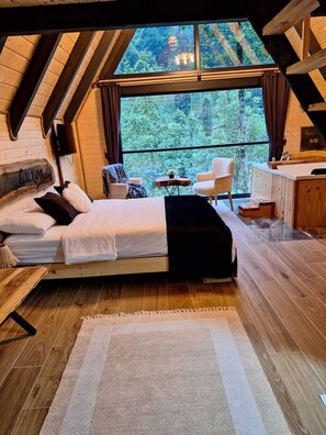 Ett mysigt sovrum på loftvåningen med ett stort fönster, en säng, en stol och ett litet bord.