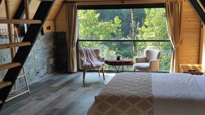 A cozy bedroom with a bed, two chairs, a small table, and a window with a view of trees. - Luxon Suit Bungalov (Camlihemsin)