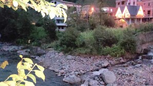 A river with rocks and a small waterfall, surrounded by greenery and buildings in the background. - Luxon Suit Bungalov (Camlihemsin)