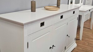 Un mueble blanco con varios cajones y puertas, un cuadro en la pared, y piso de madera.