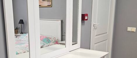 A white bedside table with a mirror, a small bedside lamp, and a framed picture on the wall.