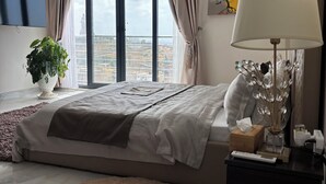 A modern bedroom with a large bed, a round rug, a bedside table with a lamp, and a view of the city through large windows. - TERANGA ROOF TOP Exceptional seaside apartment (Dakar)