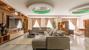 A modern living room with a large sectional sofa, a flat-screen TV, wooden shelving, and a ceiling with circular green lighting. - TERANGA ROOF TOP Exceptional seaside apartment (Dakar)