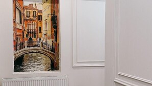 A hallway with a large framed painting of a canal scene, a white radiator, and a red fire extinguisher. - Aniko Hotel (Batumi)