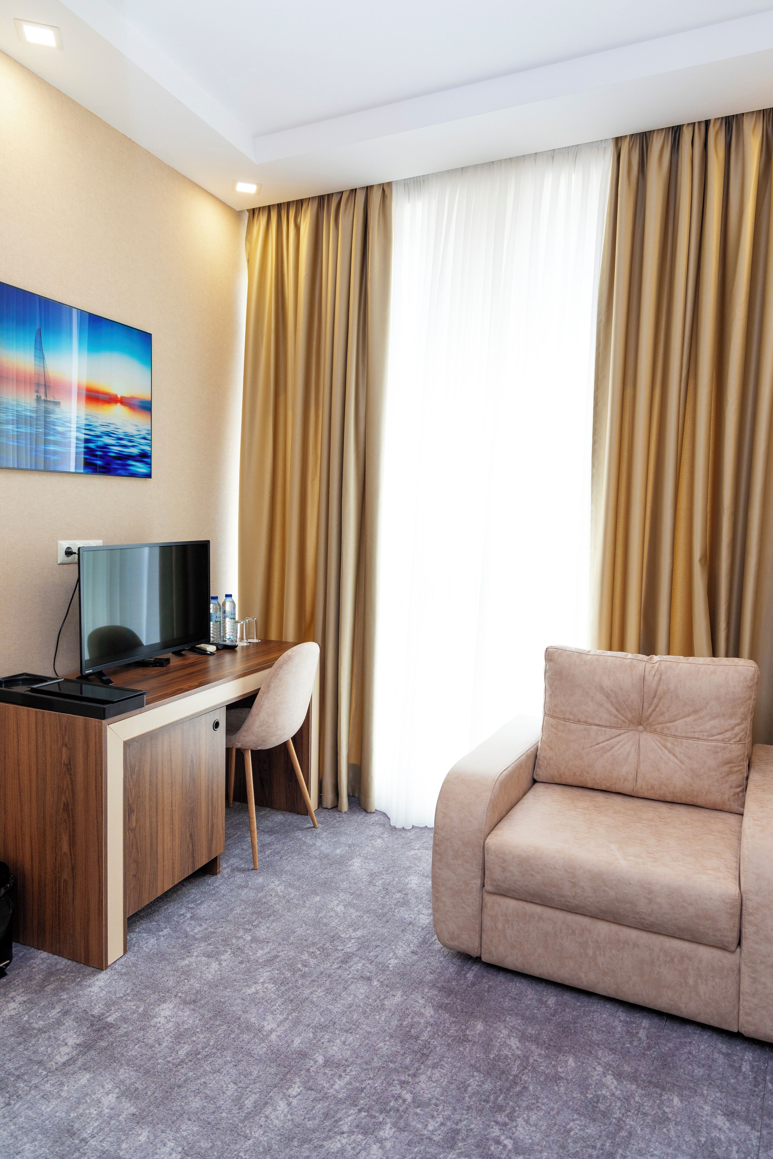 Una habitación de hotel con un escritorio de madera, un sofá color beige, una televisión y un cuadro en la pared.