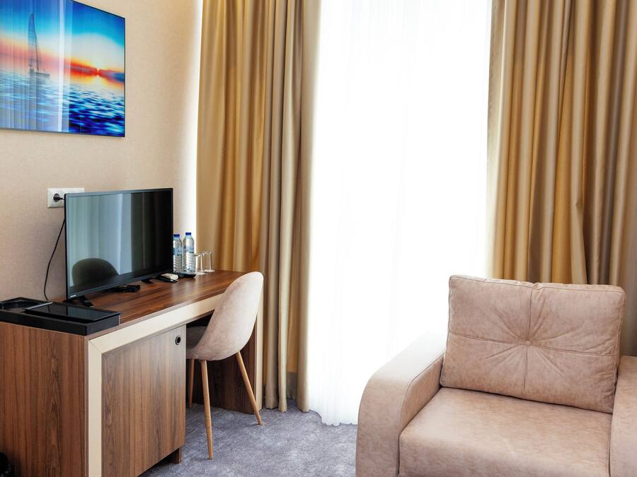Una habitación de hotel con un escritorio de madera, un sofá color beige, una televisión y un cuadro en la pared.