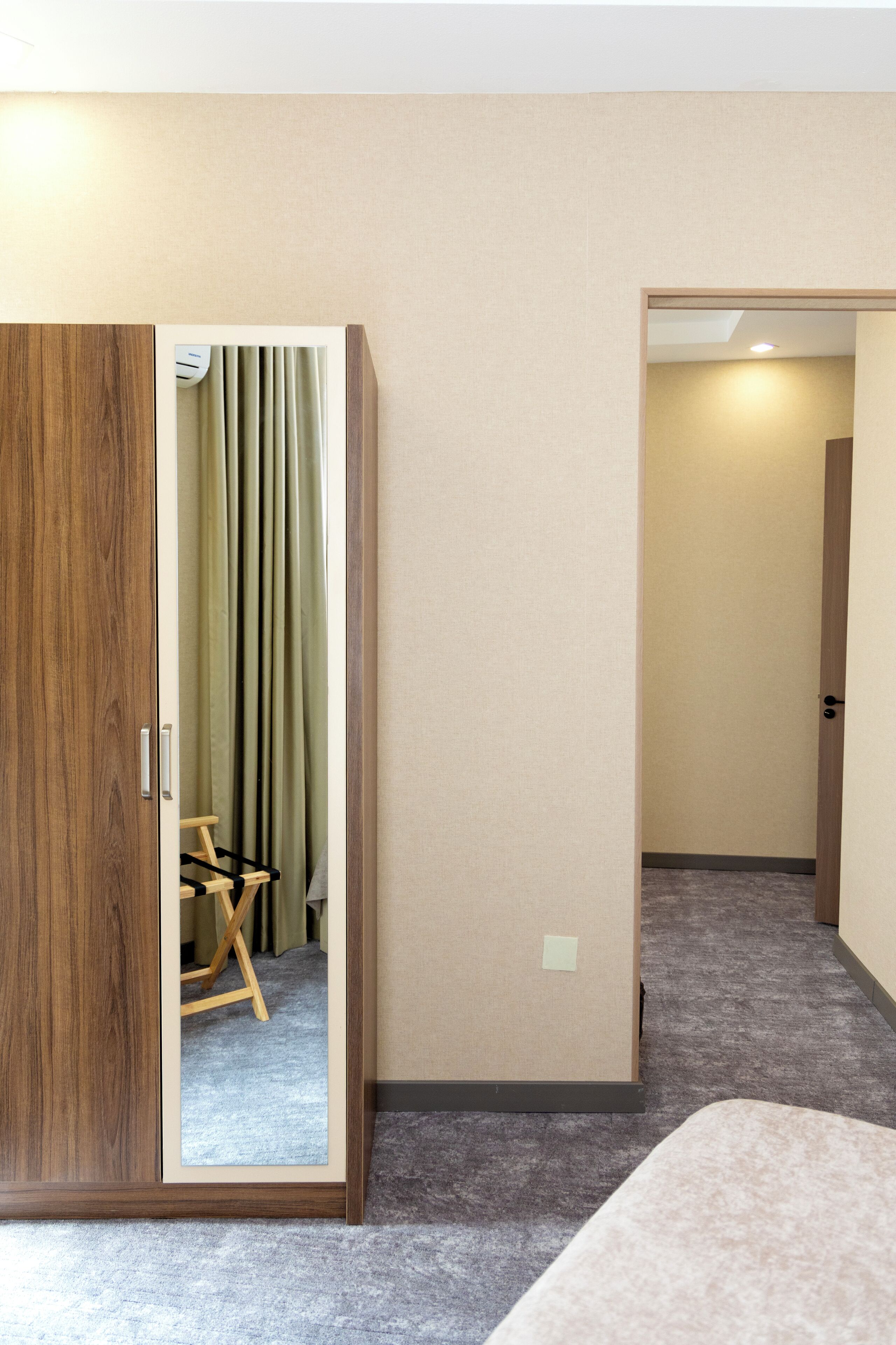 Une chambre d’hôtel avec une armoire en bois, une petite chaise en bois et un tapis gris.