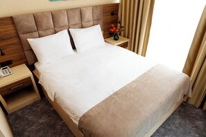 A hotel room with a large bed, a bedside table with a lamp, and a nightstand with a phone. - Aniko Hotel (Batumi)