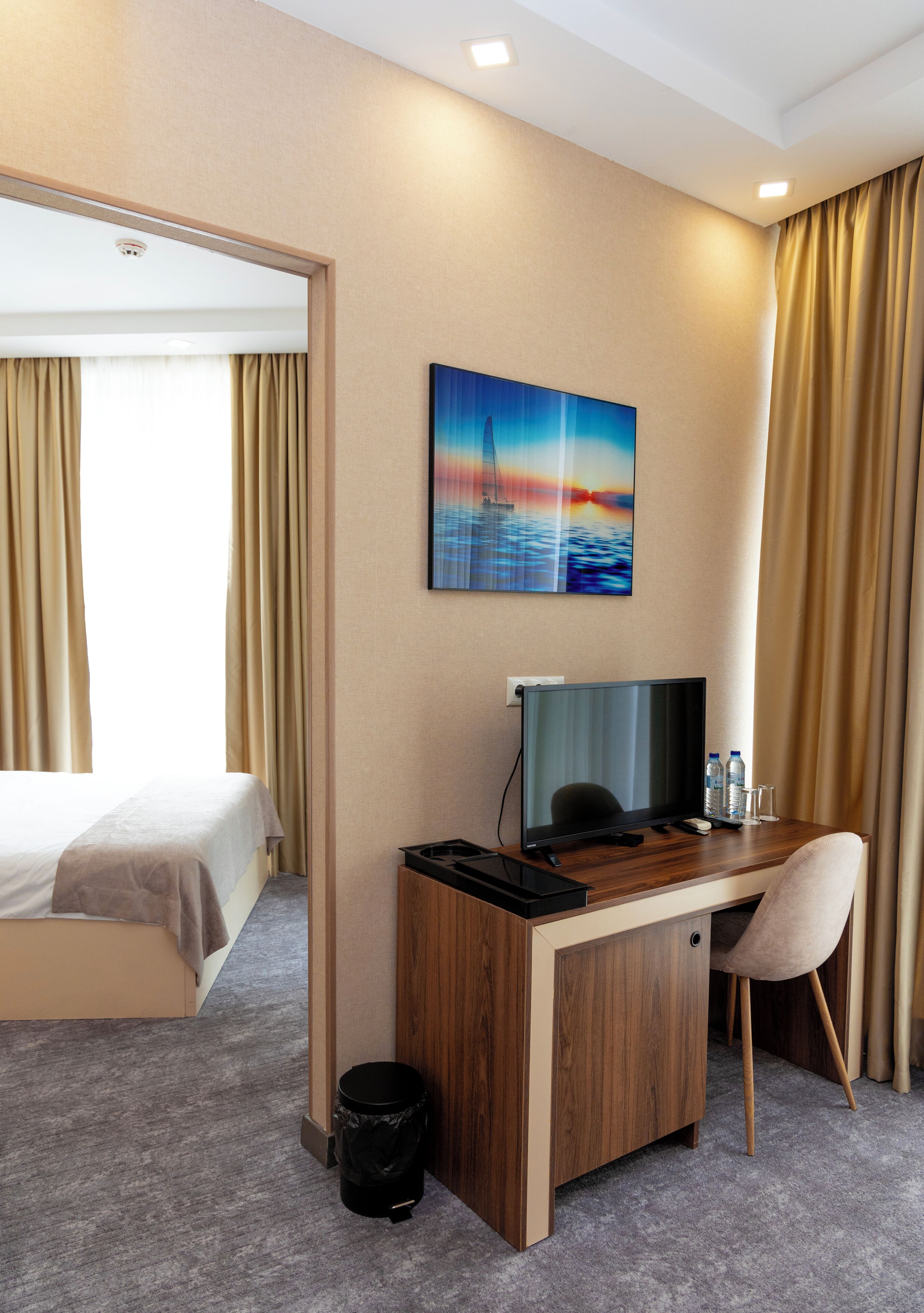 A hotel room with a bed, desk, chair, and a painting on the wall.