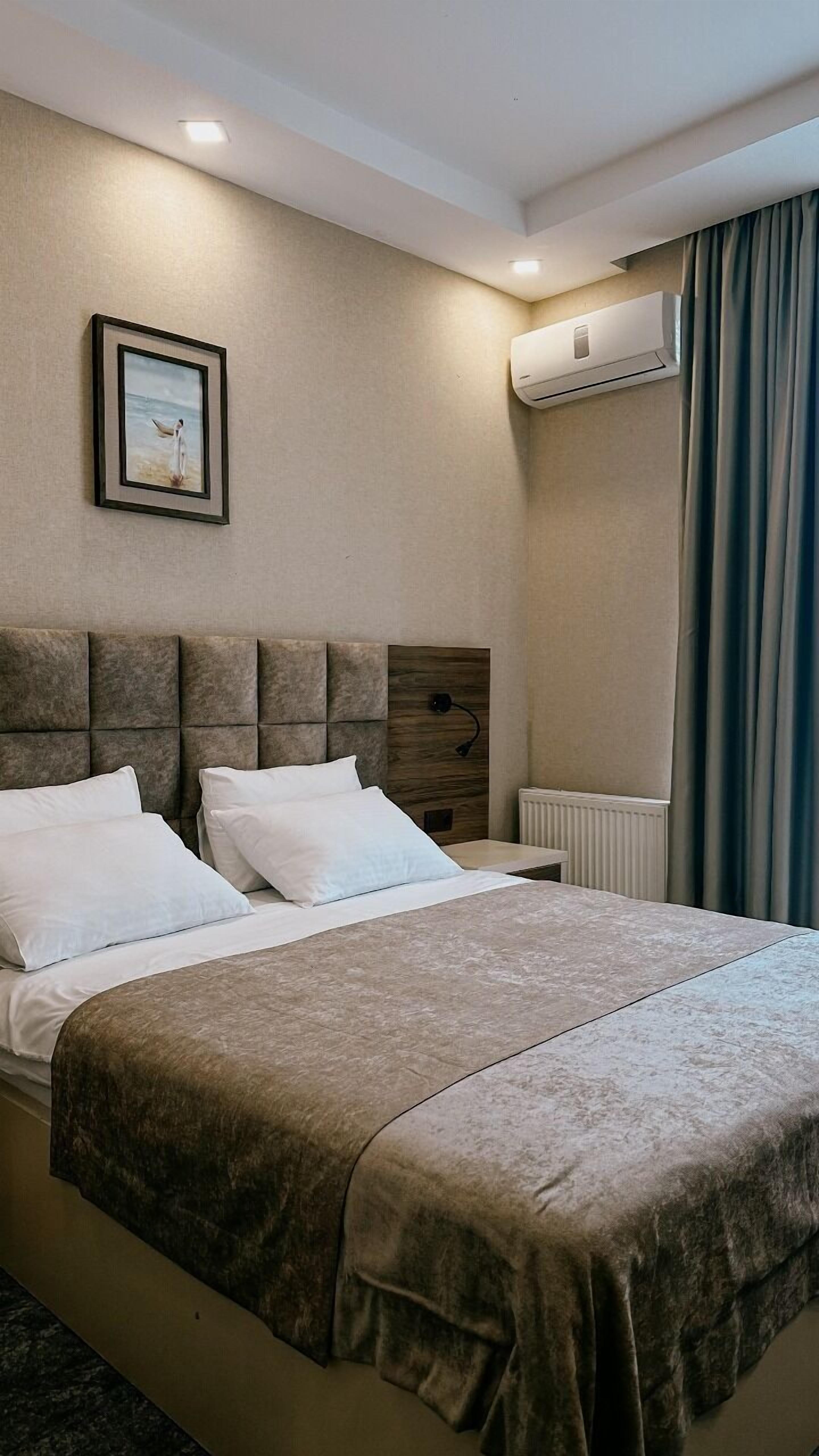 Une chambre d’hôtel avec un lit, un tableau encadré au mur, un appareil de climatisation et une fenêtre avec des rideaux.