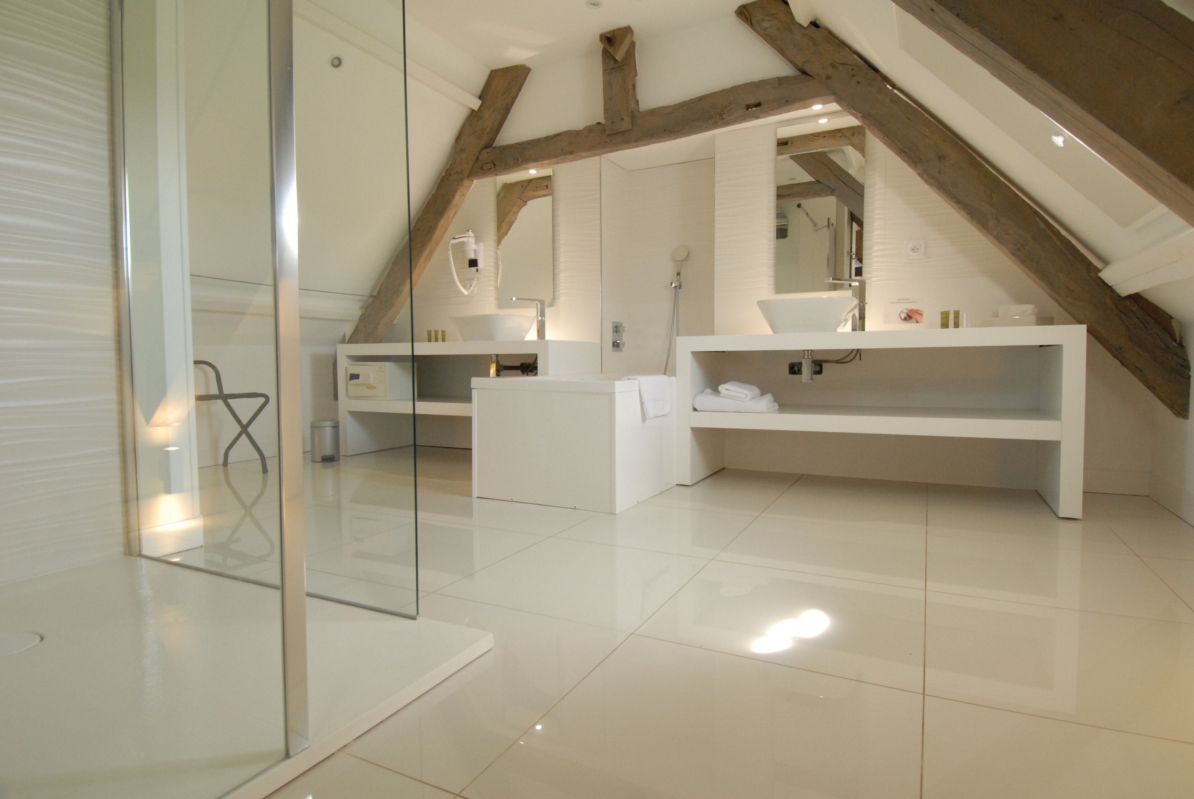 Ein modernes Badezimmer mit Duschkabine aus Glas, weißen Armaturen und freiliegenden Holzbalken.