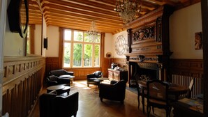 Una habitación amplia con paneles de madera, una chimenea, un reloj grande y varias zonas de estar.