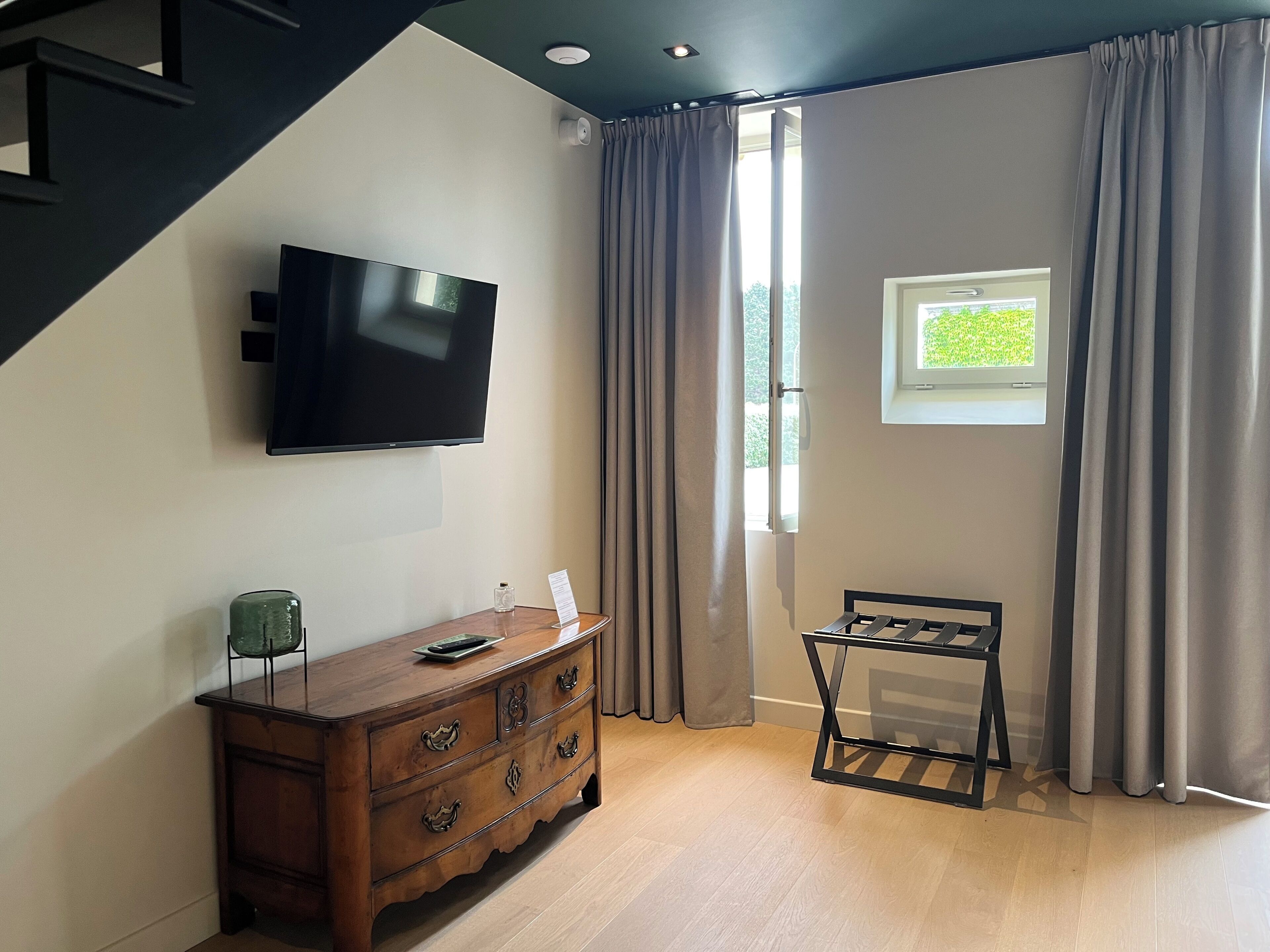 A room with a wooden dresser, a flat-screen TV, a small table, and a window with curtains.