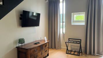 A room with a wooden dresser, a flat-screen TV, a small table, and a window with curtains.
