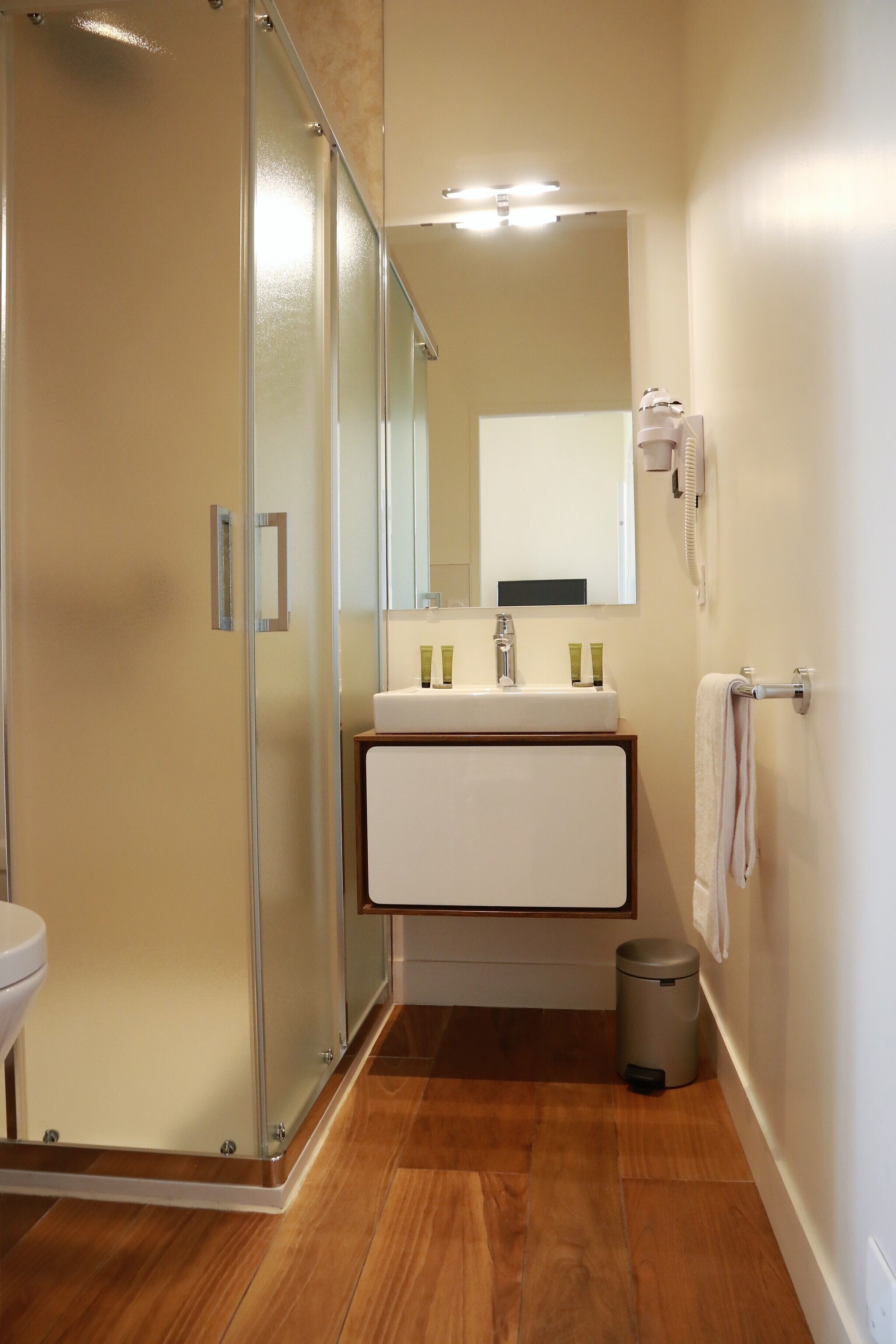 Une salle de bain moderne avec une douche à parois de verre, un lavabo blanc agrémenté d’articles de toilette verts et un miroir au-dessus du lavabo.