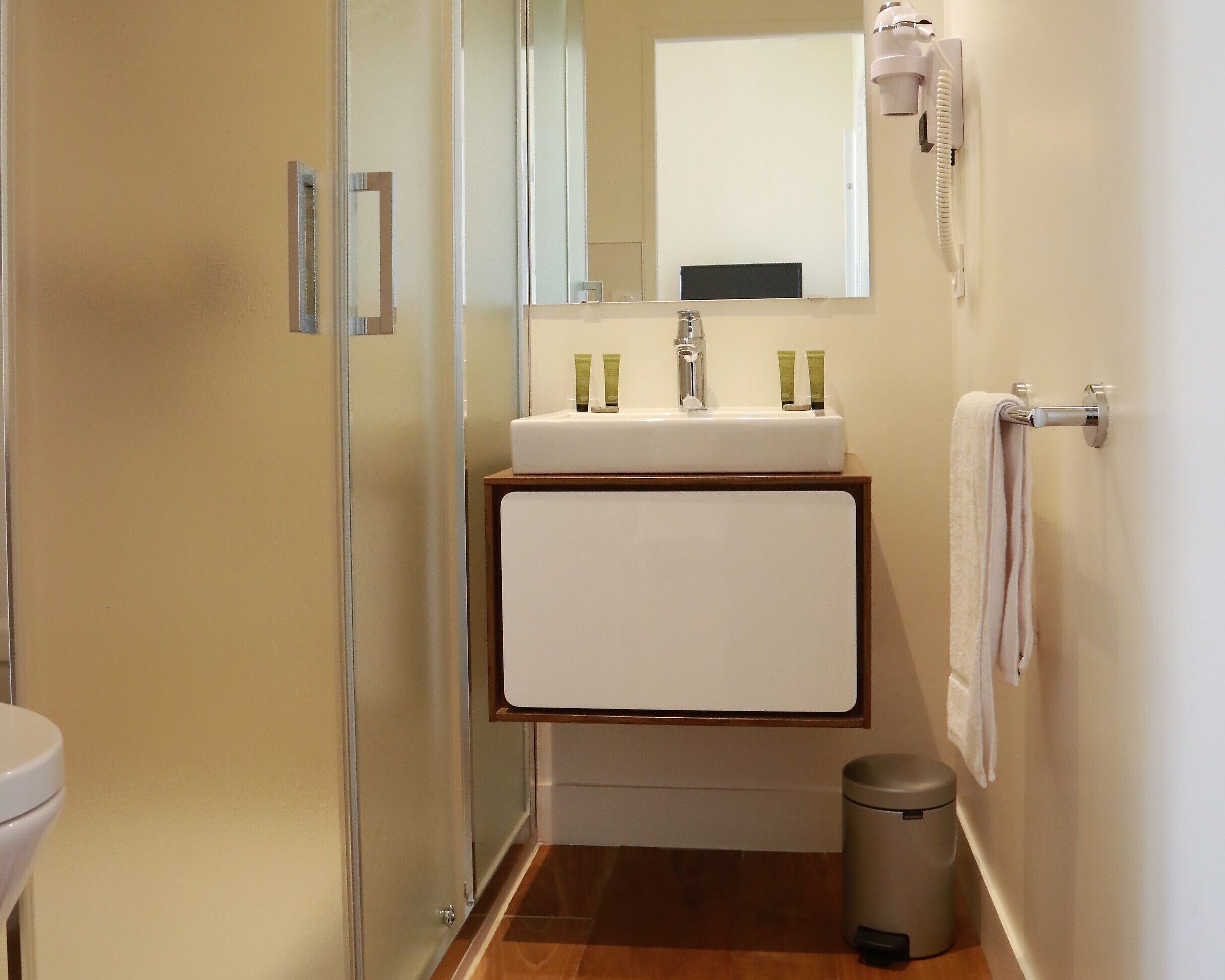 A compact bathroom with a glass shower door, a white sink with a mirror above it, and a towel rack on the wall.