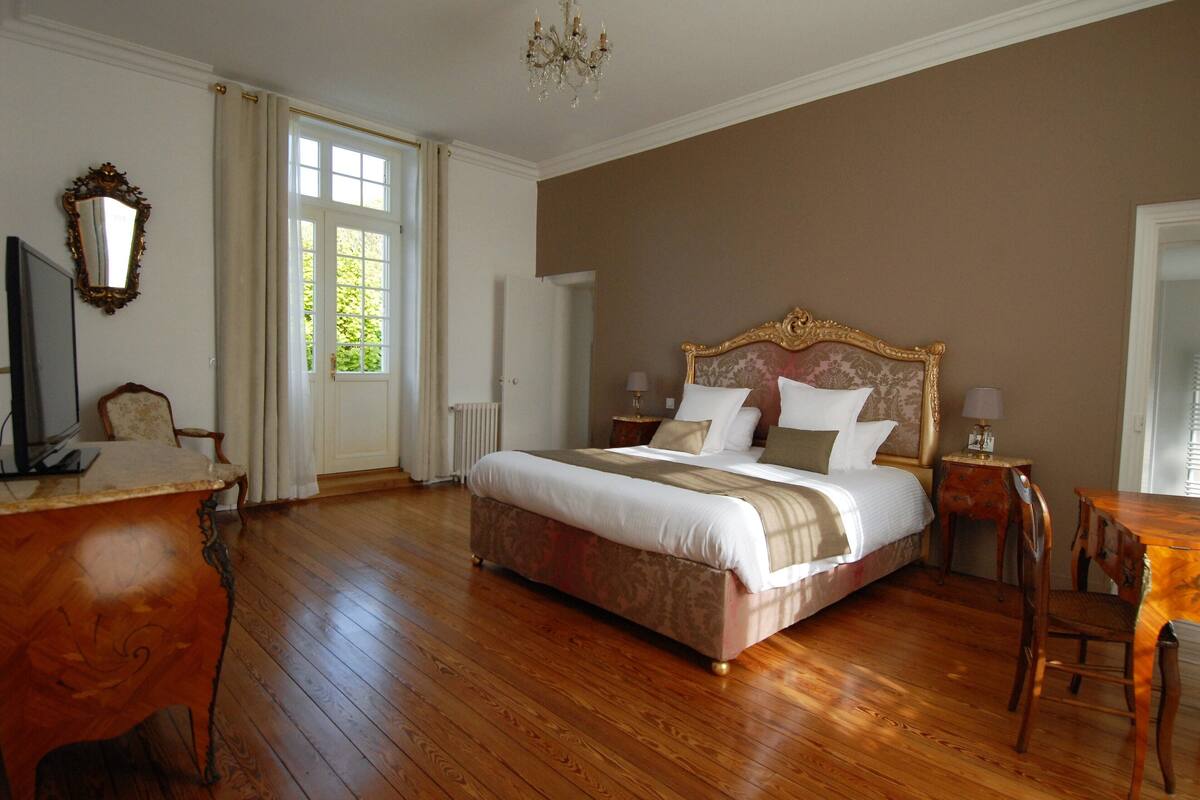 Un dormitorio espacioso con una cama grande, piso de madera, un escritorio y una silla.