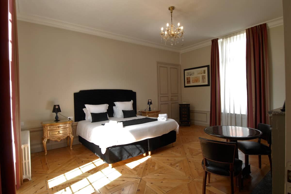Una habitación de hotel con una cama grande, una mesa redonda de comedor y un candelabro.