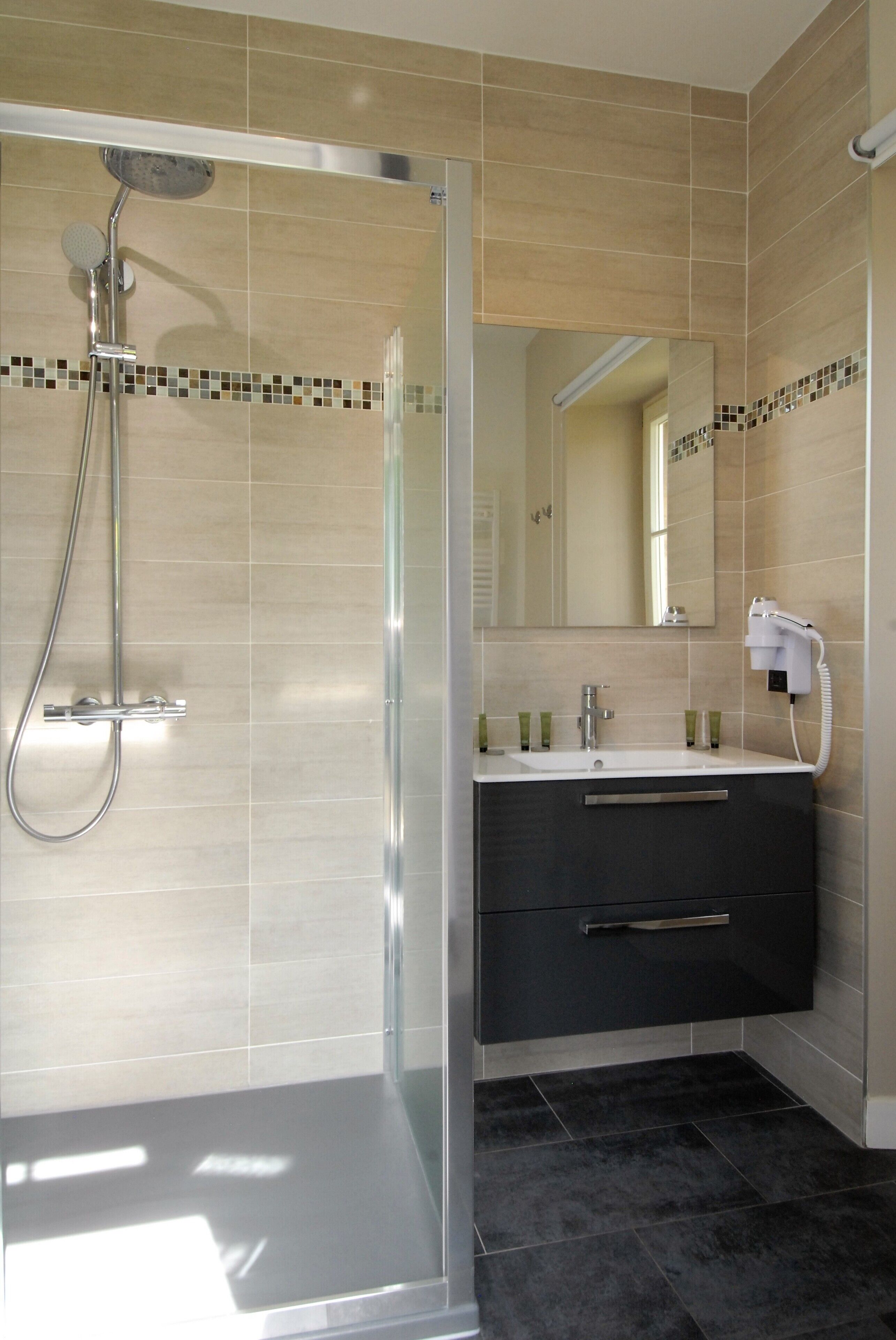 A modern bathroom with a glass-enclosed shower, a vanity with a mirror, and a hairdryer on the wall.
