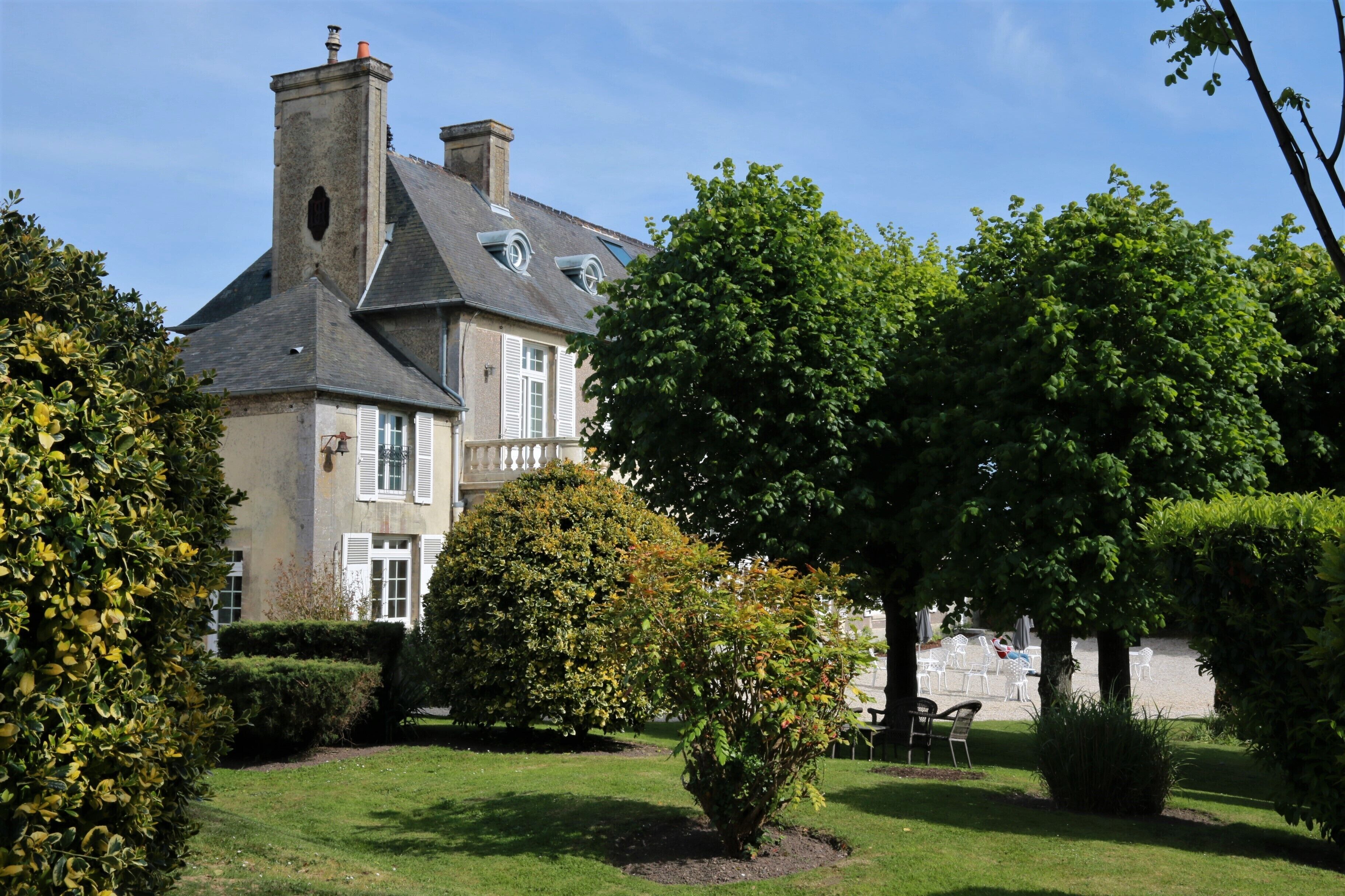 A large, historic house with a prominent chimney, surrounded by well-maintained lawns and mature trees.