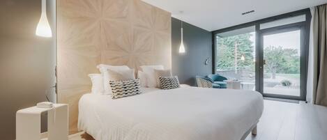 A modern bedroom with a large bed, a wooden accent wall, and a view of the outdoors.