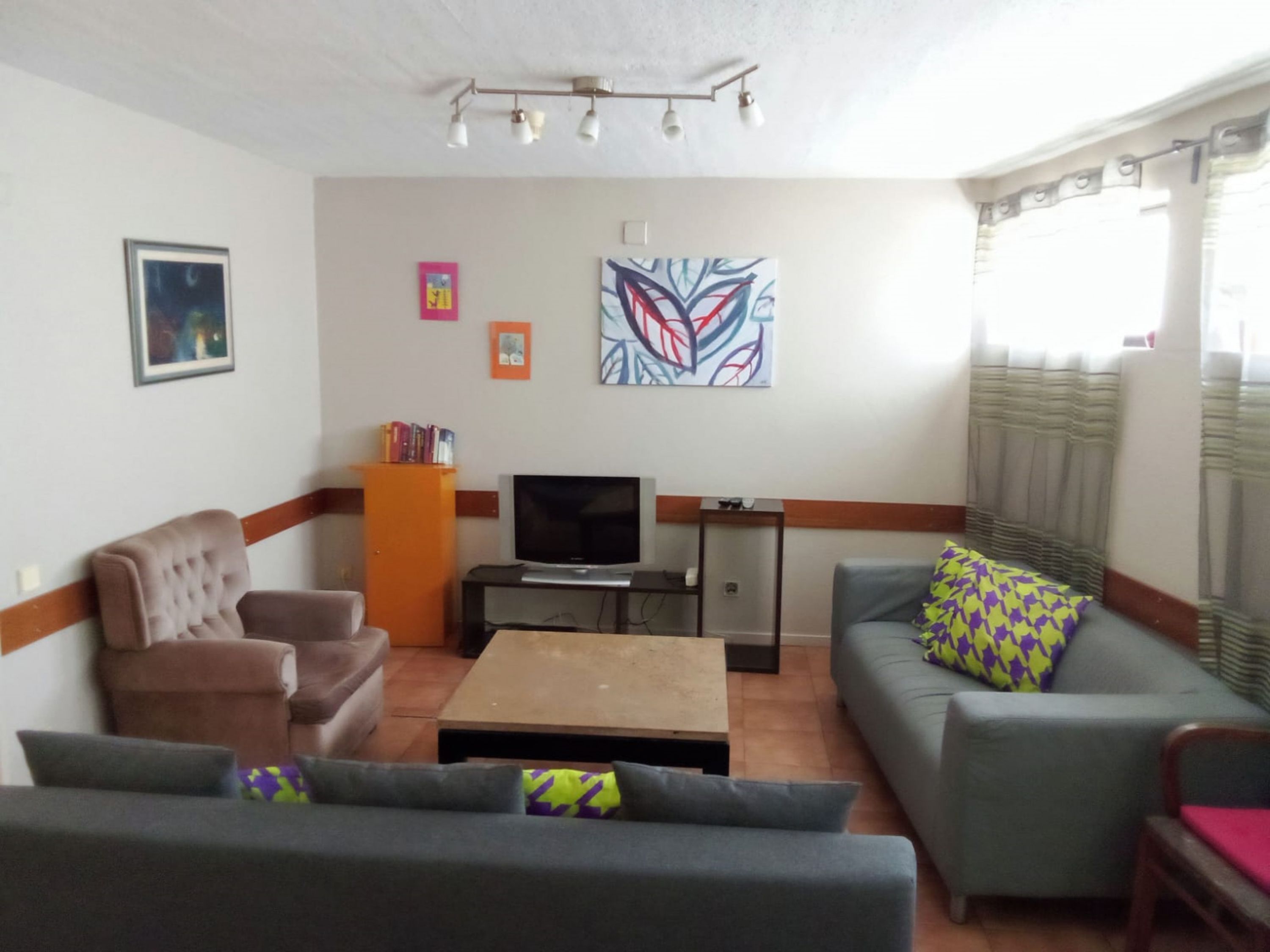 A living room with a sofa, armchair, and a coffee table. There is a television and a bookshelf with books.