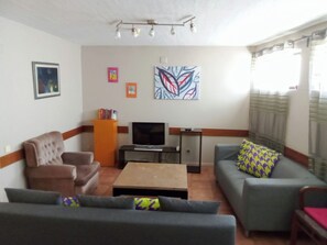 A living room with a sofa, armchair, and a coffee table. There is a television and a bookshelf with books. - Apartamento Doria - Center Porto Economic Huge Fla (Porto)