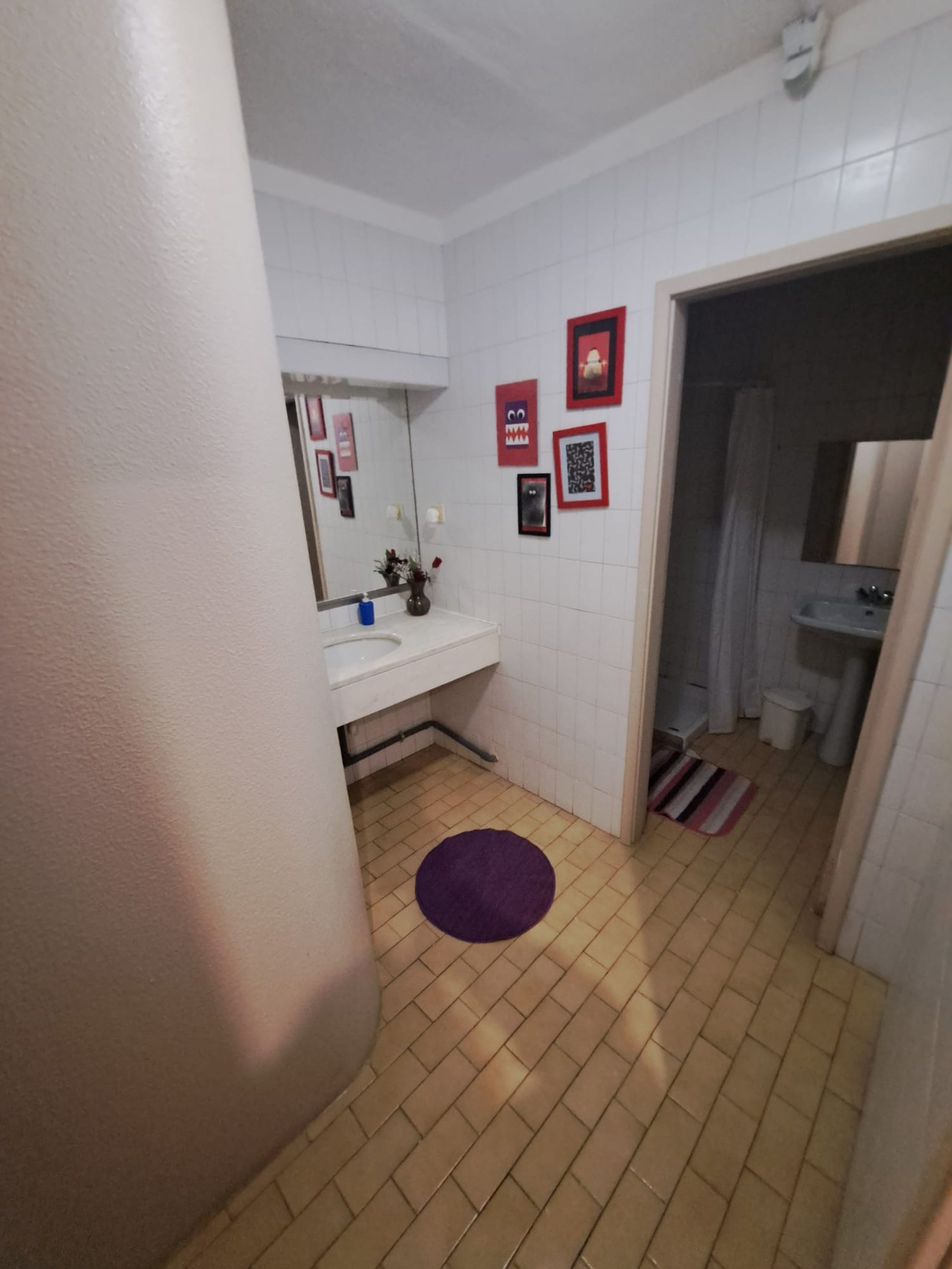 A bathroom with a white sink, mirror, and tiled walls. There are framed pictures on the wall and a purple rug on the floor.