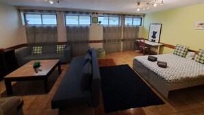 A cozy living room with a sofa, a small table, a bed, and a desk. There are curtains on the windows, and a clock is visible on the wall. - Apartamento Doria - Center Porto Economic Huge Fla (Porto)