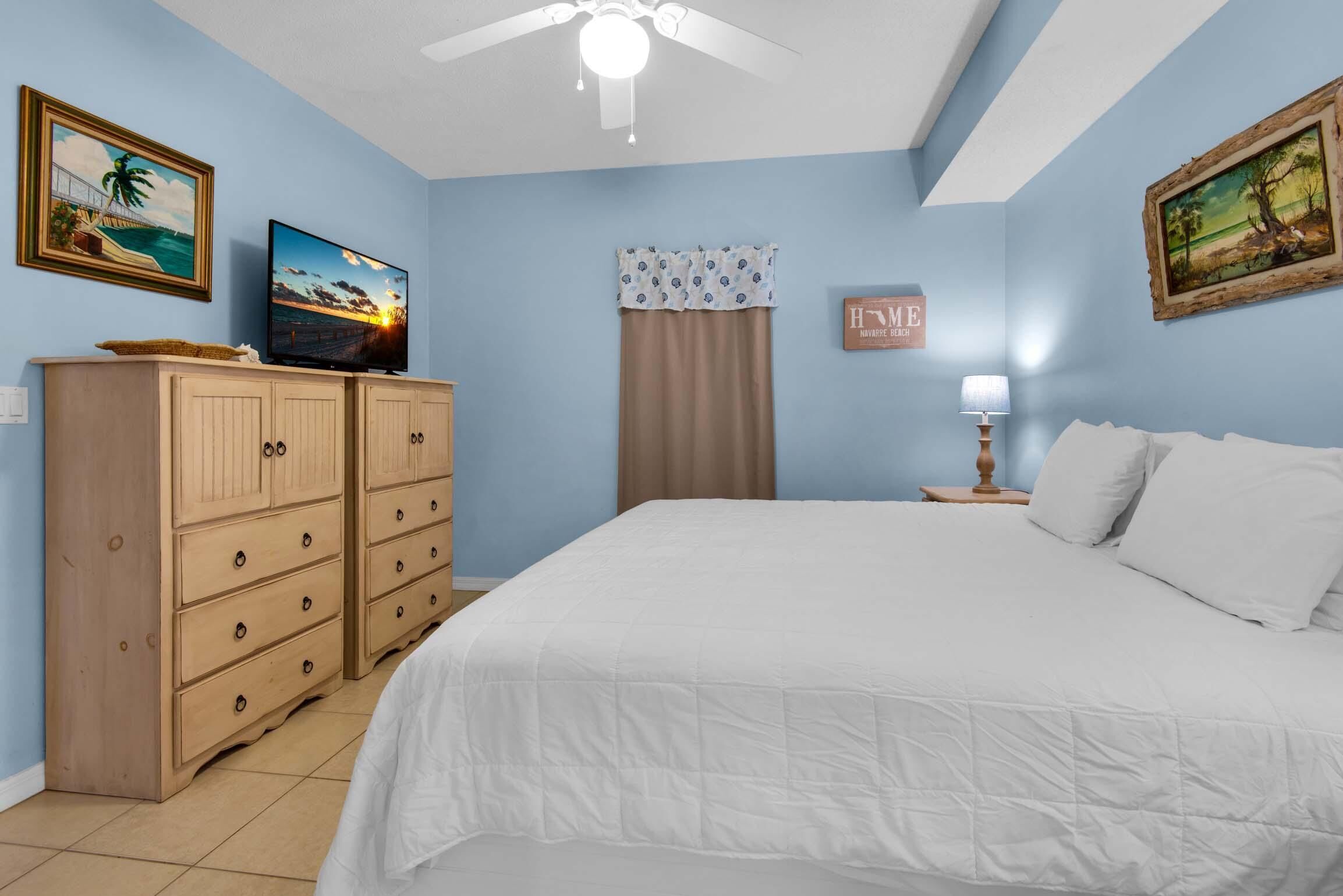 Een slaapkamer met een bed, een televisie, een plafondventilator en een nachtkastje.