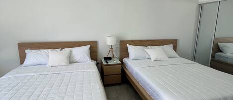 Una habitación de hotel con dos camas, una mesita de noche con lámpara, un equipo de aire acondicionado y un espejo.